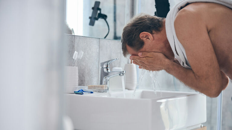 man washing face in a bathroom sink