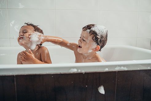 Two small children playing with bubbles in the bath.