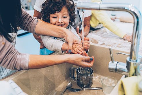 Mother and daughter washing hands together at a sink.